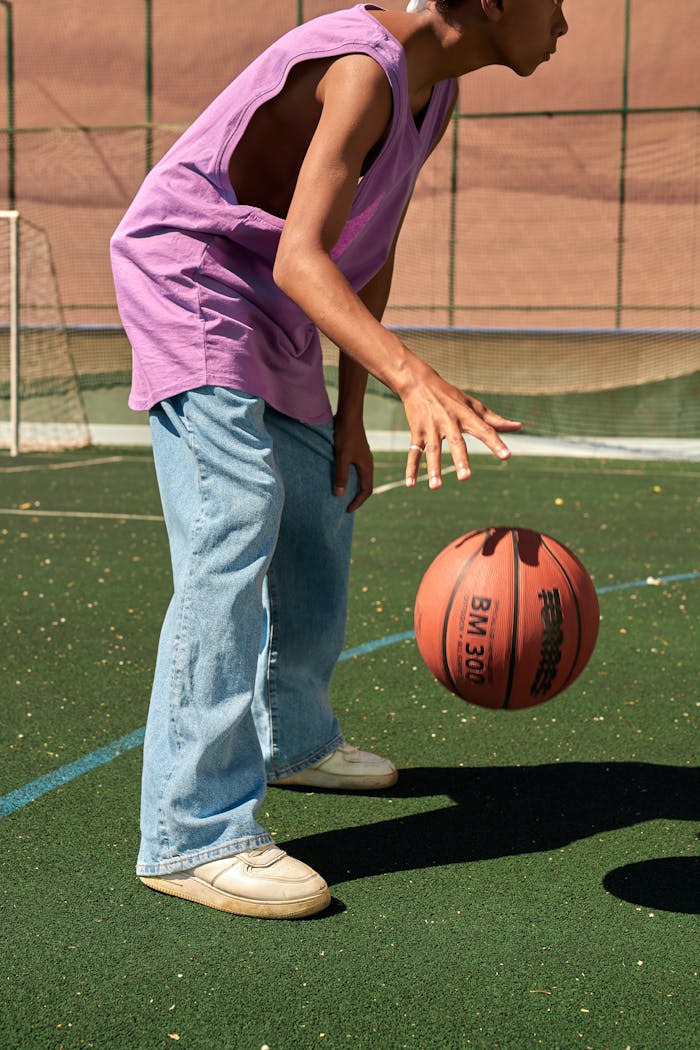 Teen dribbling a basketball on an outdoor court on a sunny day.